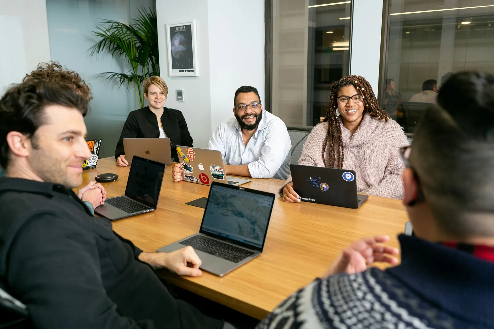 Five people talking around a meeting table with open laptops