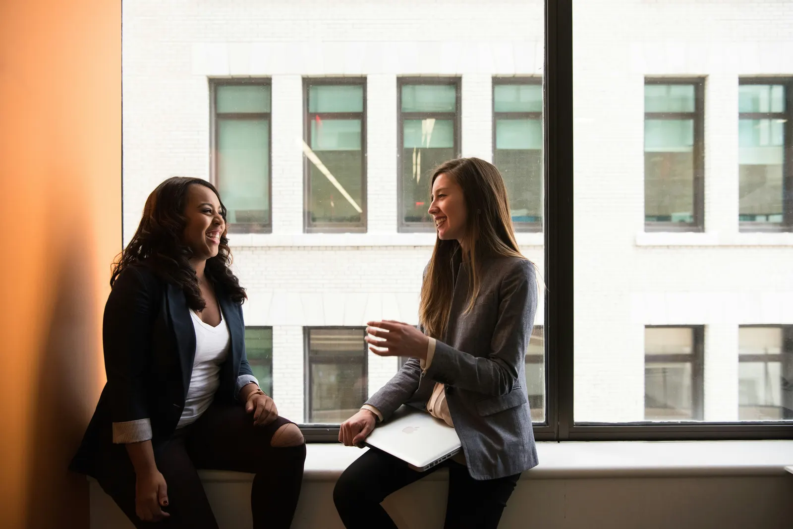 Two women talking and laughing by a bright window